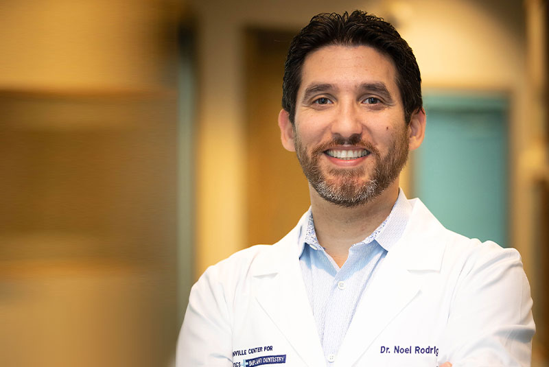 Dr. Noel Rodriguez smiling in a white coat, expert in implant and cosmetic dentistry