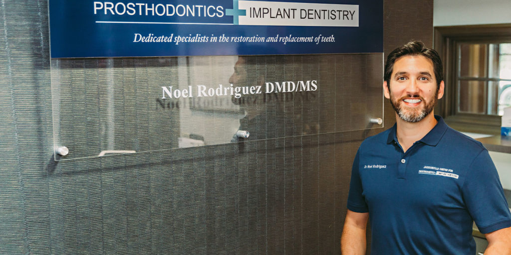 Dr. Noel Rodriguez standing in front of Jacksonville Center for Prosthodontics and Implant Dentistry signage