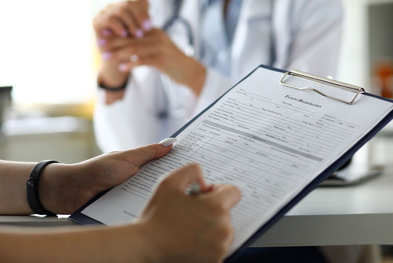 Close-up of patient filling out a registration form on a clipboard at a dental or medical office