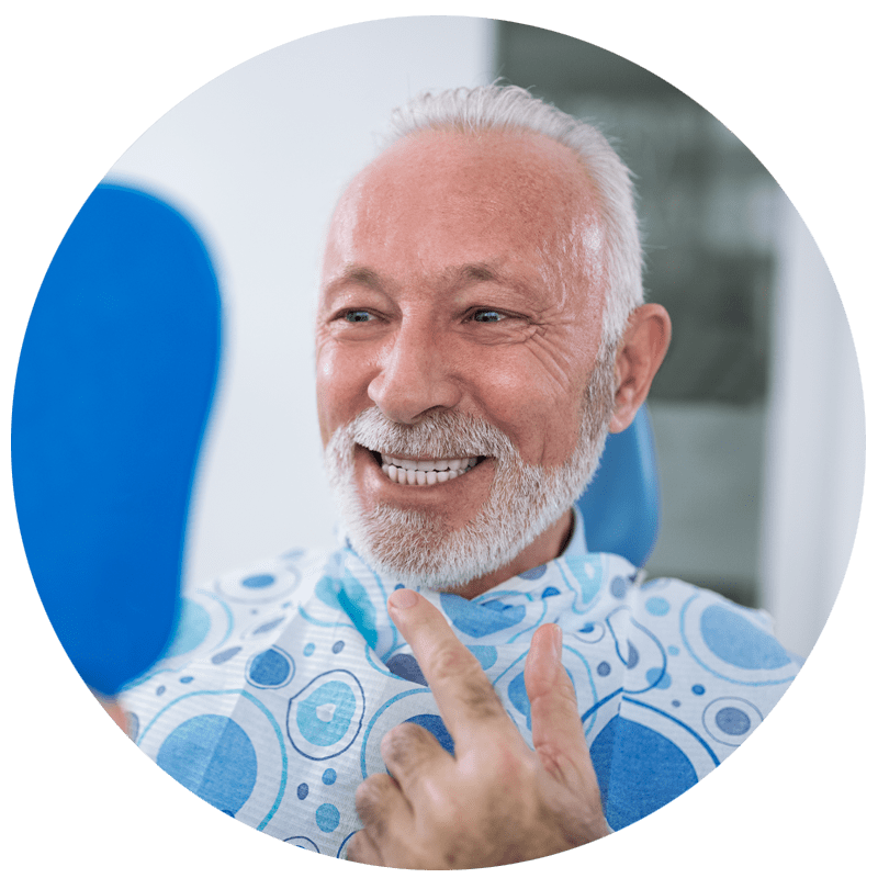 Older man smiling in dental chair while looking in mirror after dental treatment